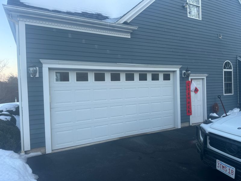 White double garage door with top windows on blue colonial home in winter snow