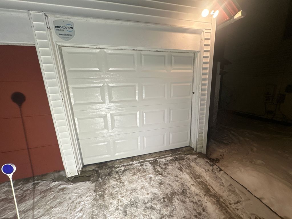 White panel garage door on detached garage illuminated at night in snow
